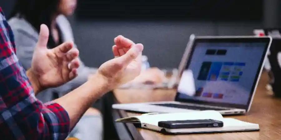 Hands gesturing in a meeting with a laptop displaying code, representing consumer tech.