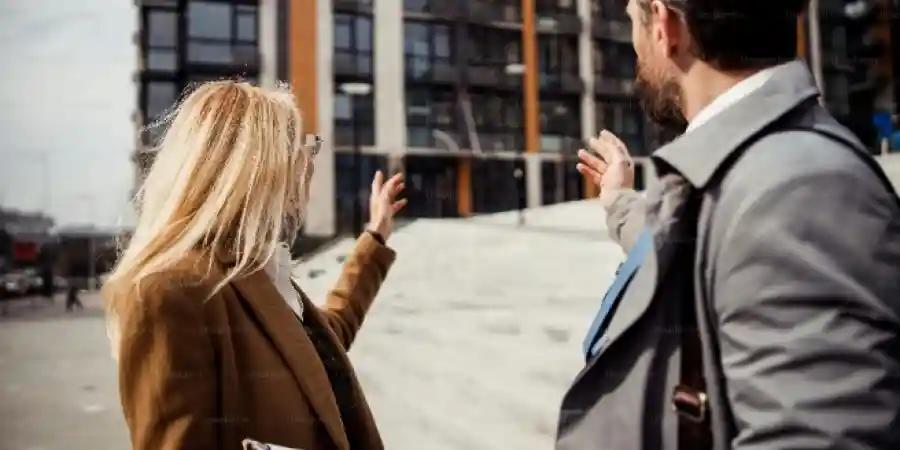Two professionals in business attire engaging in conversation outside a modern office building, symbolising real estate.