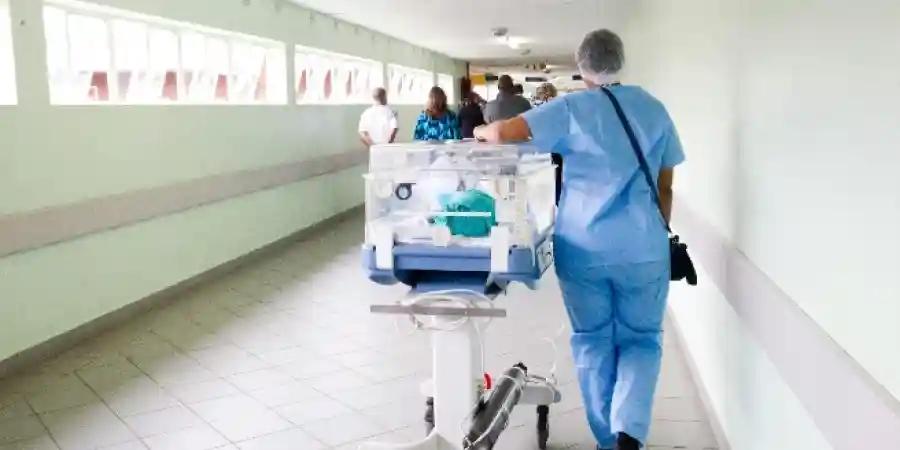 A healthcare professional pushing a newborn in an incubator through a hospital corridor